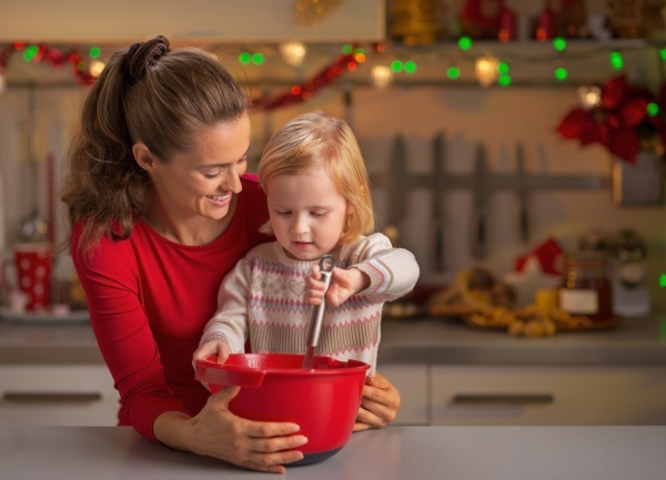 Happy mother and baby whisking dough in christmas decorated kitchen